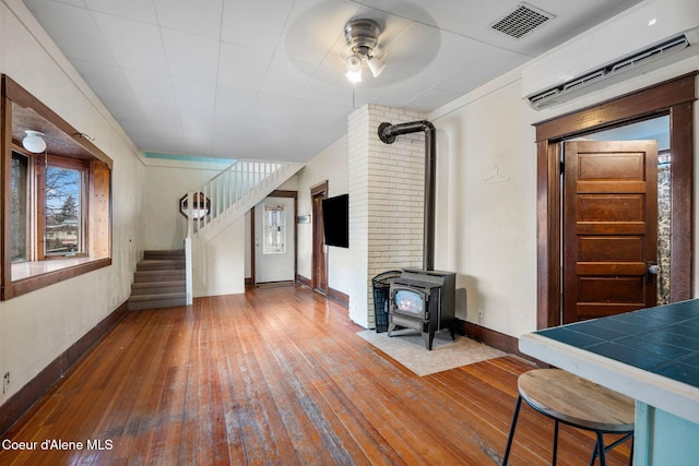 unfurnished living room with ceiling fan, a wall mounted air conditioner, a wood stove, and hardwood / wood-style floors