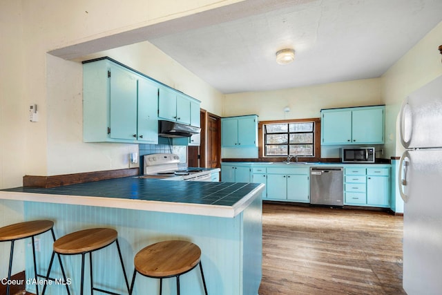 kitchen with white appliances, kitchen peninsula, blue cabinetry, and hardwood / wood-style floors