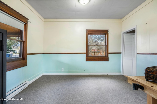 carpeted spare room with a baseboard heating unit, crown molding, and a wealth of natural light