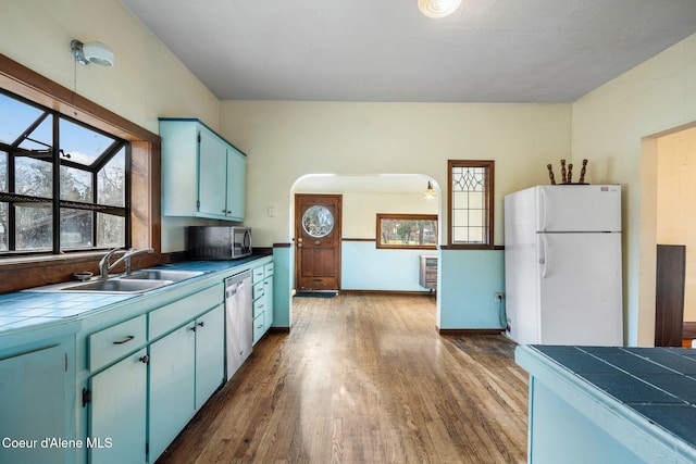 kitchen with appliances with stainless steel finishes, dark wood-type flooring, sink, and tile counters