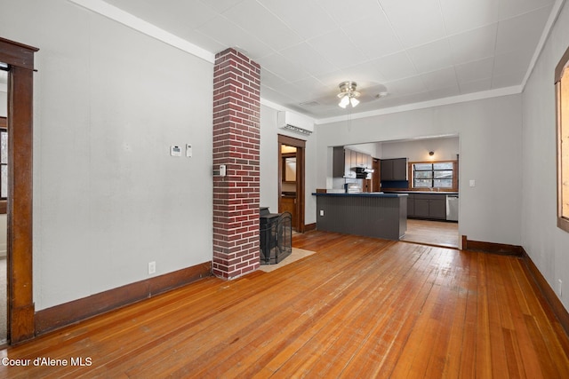 unfurnished living room featuring light wood-type flooring, a wall mounted air conditioner, a wood stove, and baseboards