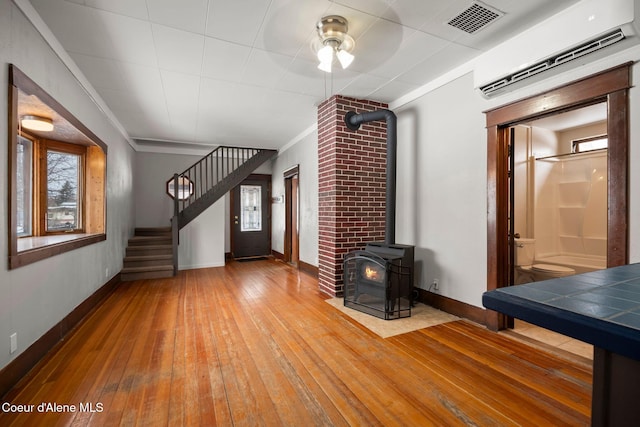 unfurnished living room featuring visible vents, baseboards, stairs, light wood-type flooring, and a wood stove