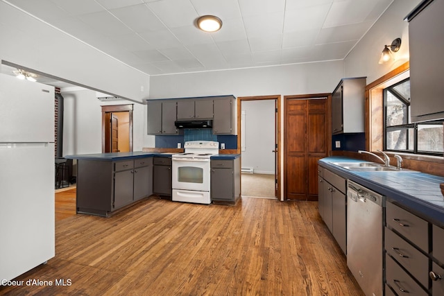 kitchen with white appliances, dark countertops, a sink, and gray cabinetry