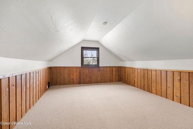 bonus room with a wainscoted wall, wood walls, lofted ceiling, and a textured ceiling