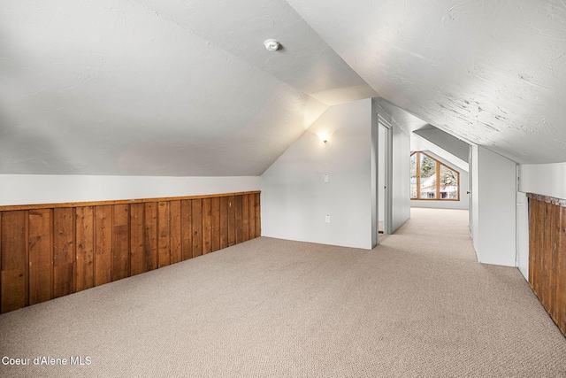 bonus room with lofted ceiling, wood walls, a textured ceiling, and light colored carpet