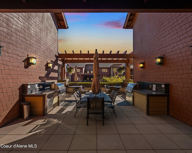 patio terrace at dusk with an outdoor kitchen, a grill, and a pergola