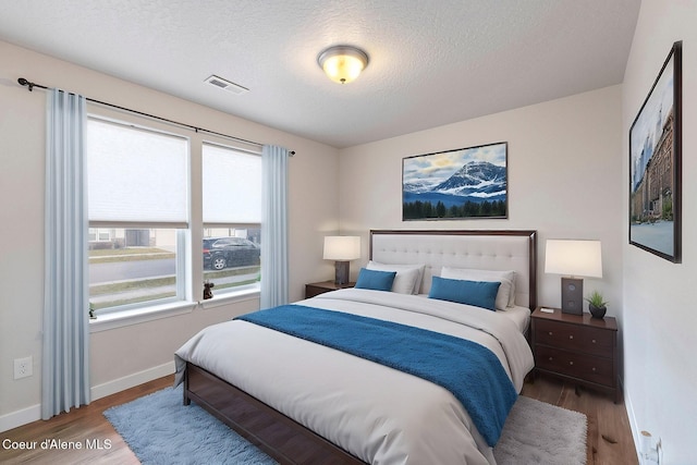 bedroom with hardwood / wood-style floors, a textured ceiling, and multiple windows