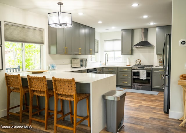 kitchen featuring pendant lighting, a breakfast bar area, wall chimney exhaust hood, kitchen peninsula, and stainless steel appliances