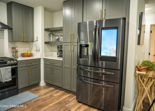 kitchen featuring gray cabinetry, wall chimney exhaust hood, gas range oven, stainless steel fridge, and hardwood / wood-style floors