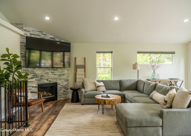 living room with hardwood / wood-style floors, a stone fireplace, and lofted ceiling