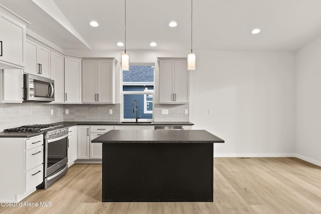 kitchen with appliances with stainless steel finishes, hanging light fixtures, a kitchen island, sink, and light hardwood / wood-style flooring