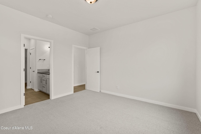 unfurnished bedroom featuring light colored carpet and ensuite bath