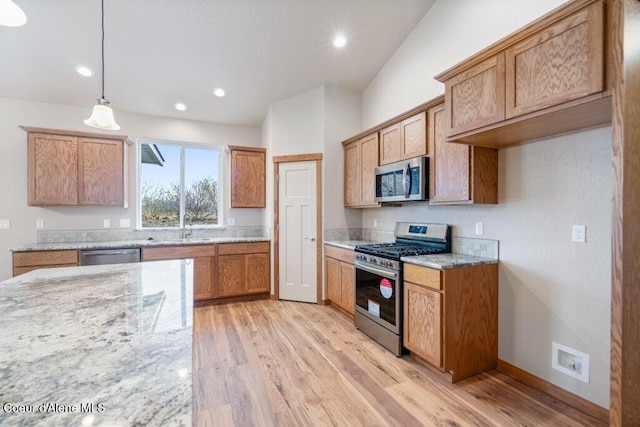 kitchen featuring sink, light hardwood / wood-style flooring, light stone countertops, pendant lighting, and appliances with stainless steel finishes