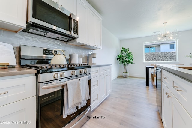 kitchen with light hardwood / wood-style floors, stainless steel appliances, a notable chandelier, white cabinets, and tasteful backsplash