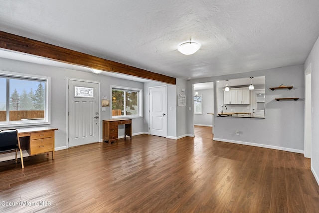 unfurnished living room featuring a textured ceiling, dark hardwood / wood-style floors, built in desk, and a healthy amount of sunlight