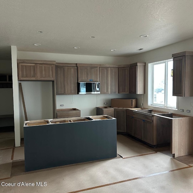 kitchen with a center island, stainless steel microwave, and a textured ceiling