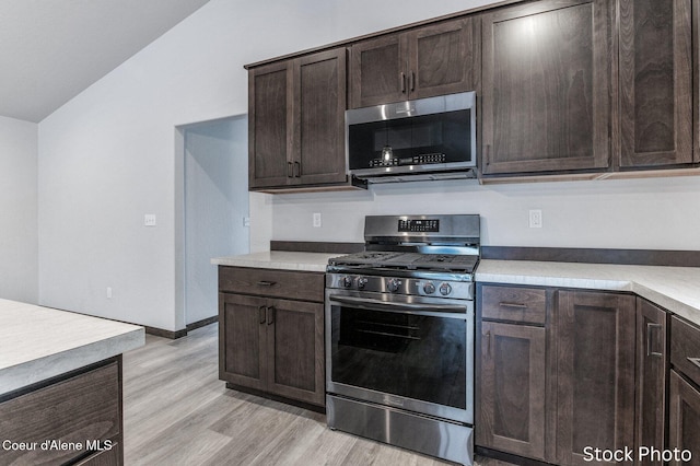 kitchen with vaulted ceiling, appliances with stainless steel finishes, dark brown cabinets, and light hardwood / wood-style floors