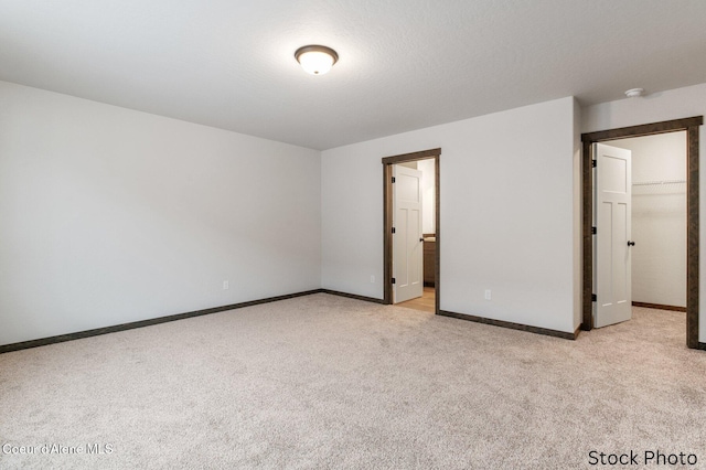 unfurnished bedroom featuring light carpet, a spacious closet, and a textured ceiling