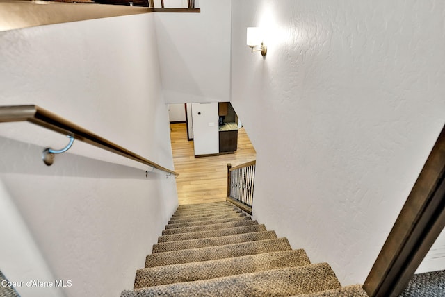 stairs featuring wood finished floors and a textured wall