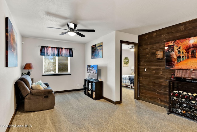 sitting room with wooden walls, a ceiling fan, baseboards, and a textured ceiling