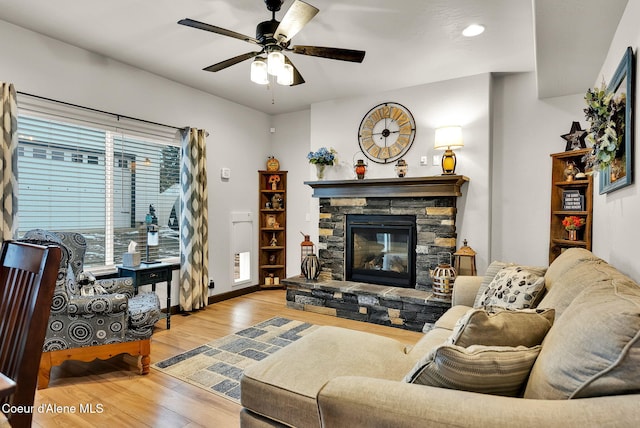 living area featuring a stone fireplace, baseboards, a ceiling fan, and wood finished floors