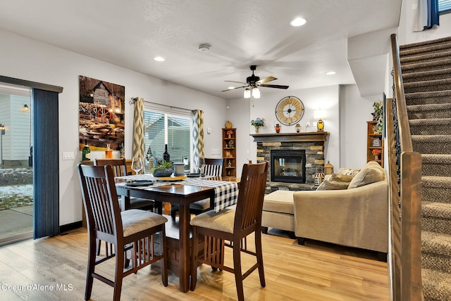 dining area featuring stairway, ceiling fan, a fireplace, and light wood finished floors