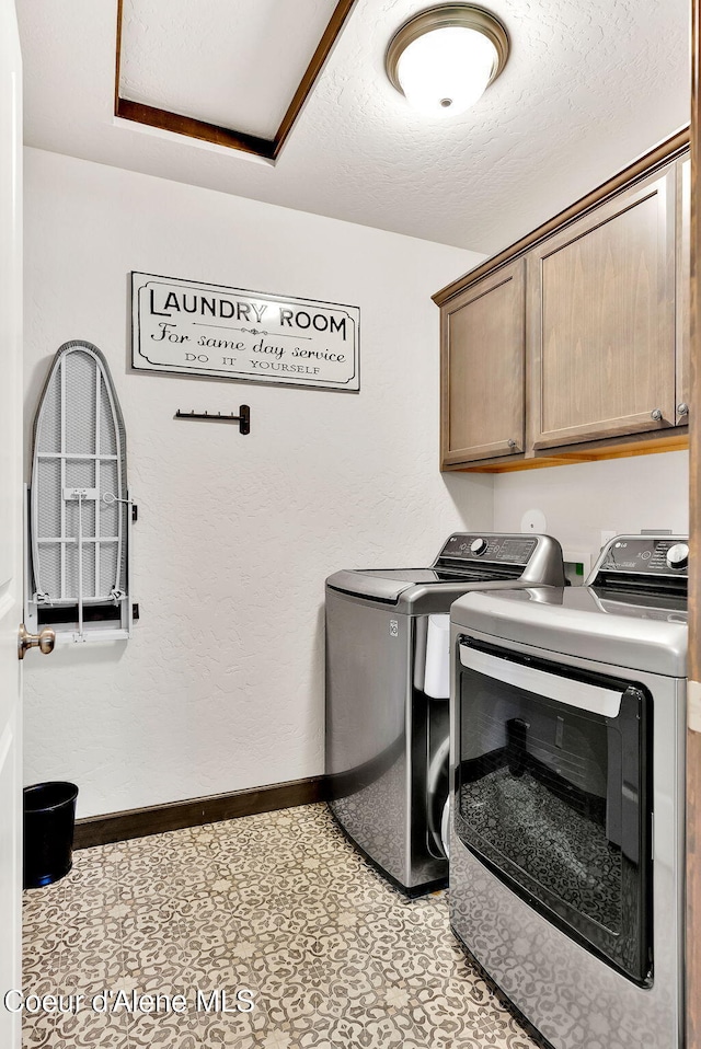 laundry area featuring light floors, baseboards, washing machine and clothes dryer, cabinet space, and a textured ceiling