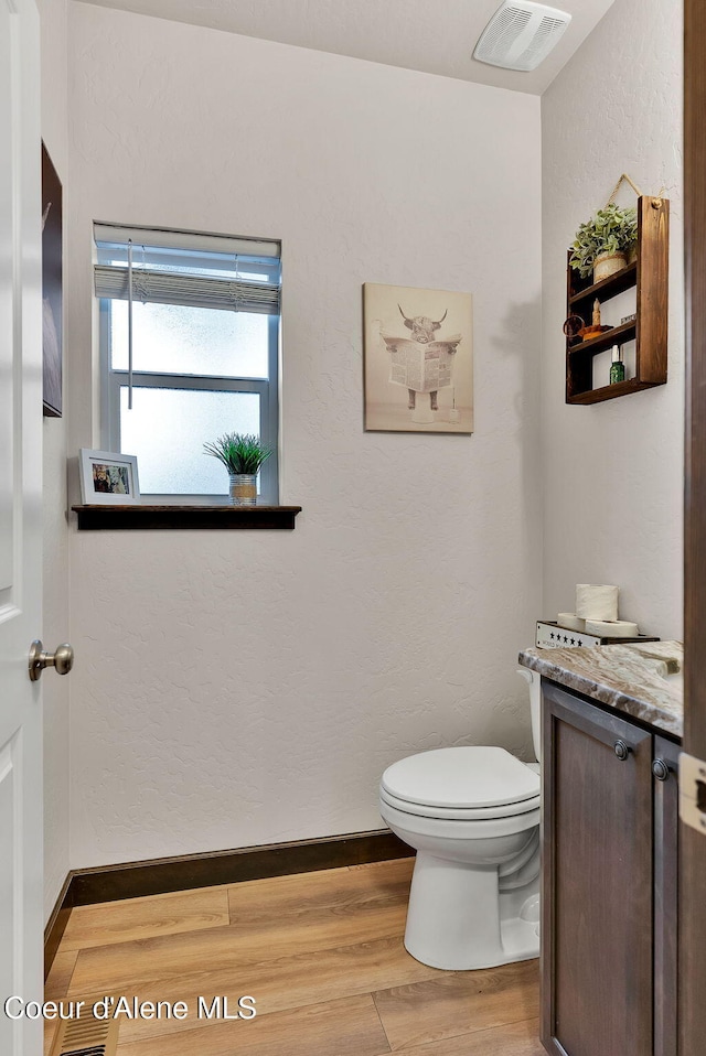 bathroom with toilet, wood finished floors, visible vents, and baseboards