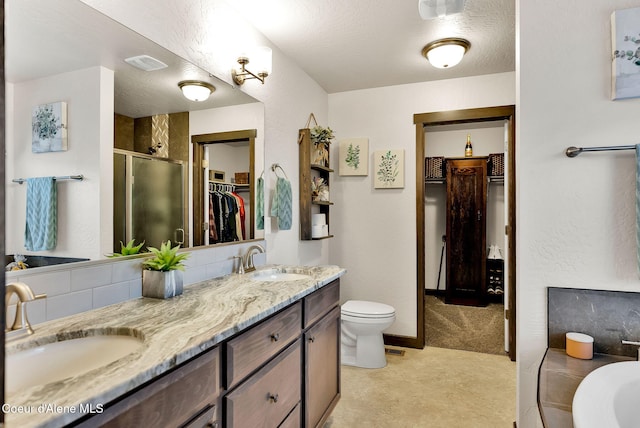 bathroom with a walk in closet, double vanity, a stall shower, and a sink