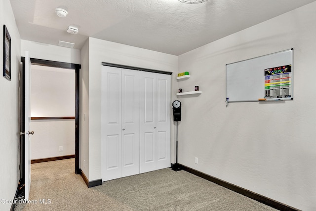 unfurnished bedroom with a closet, light colored carpet, a textured ceiling, and baseboards