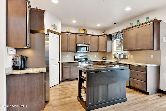 kitchen featuring a kitchen island, a sink, hanging light fixtures, stainless steel appliances, and light wood-type flooring