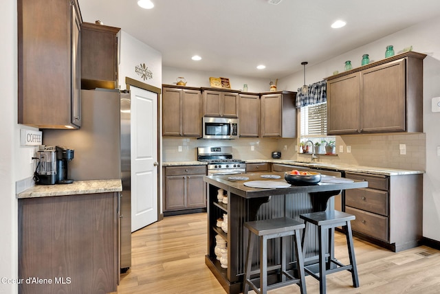 kitchen featuring light wood-style flooring, appliances with stainless steel finishes, a center island, and a sink