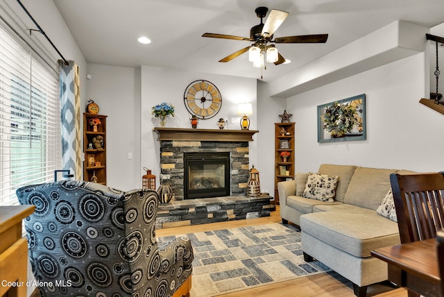 living room with a stone fireplace, recessed lighting, wood finished floors, and a ceiling fan