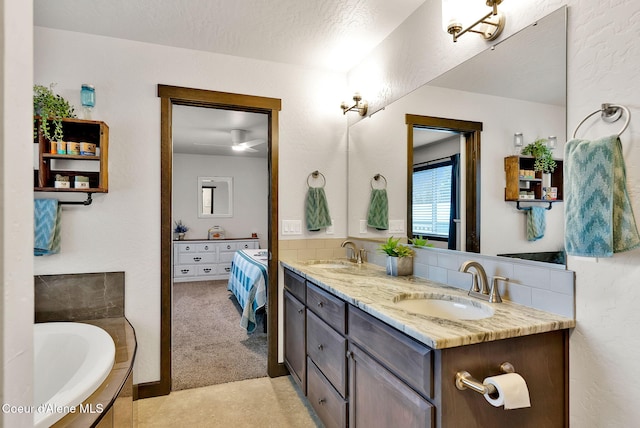 bathroom with double vanity, a washtub, a textured wall, and a sink