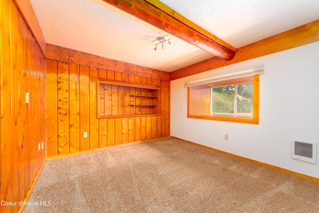 carpeted empty room featuring beam ceiling, a textured ceiling, and wooden walls