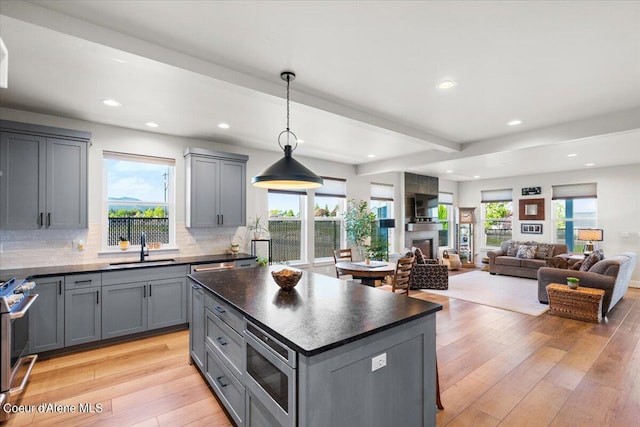 kitchen with a large fireplace, stainless steel appliances, a center island, sink, and decorative light fixtures