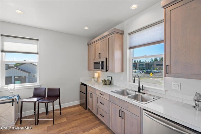 kitchen featuring appliances with stainless steel finishes, a healthy amount of sunlight, light wood-type flooring, and sink