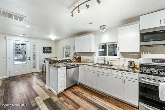 kitchen featuring appliances with stainless steel finishes, white cabinetry, dark stone counters, sink, and kitchen peninsula