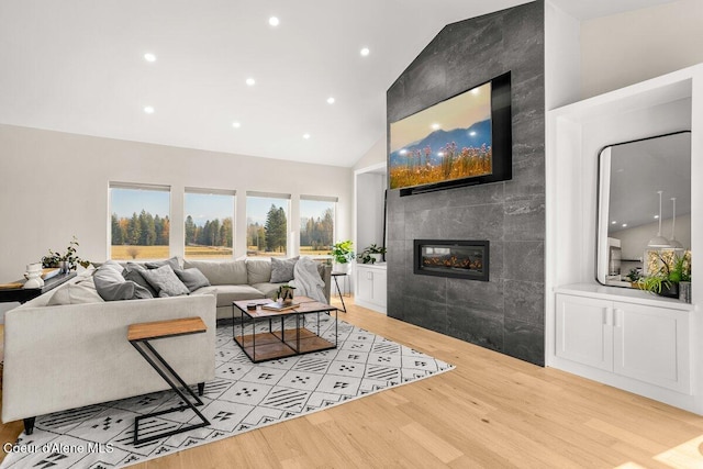 living room featuring tile walls, light wood-type flooring, high vaulted ceiling, and a fireplace