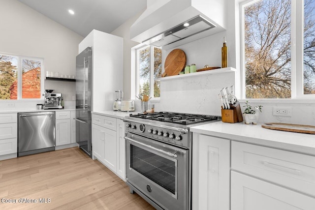 kitchen featuring white cabinets, vaulted ceiling, custom range hood, light hardwood / wood-style floors, and premium appliances