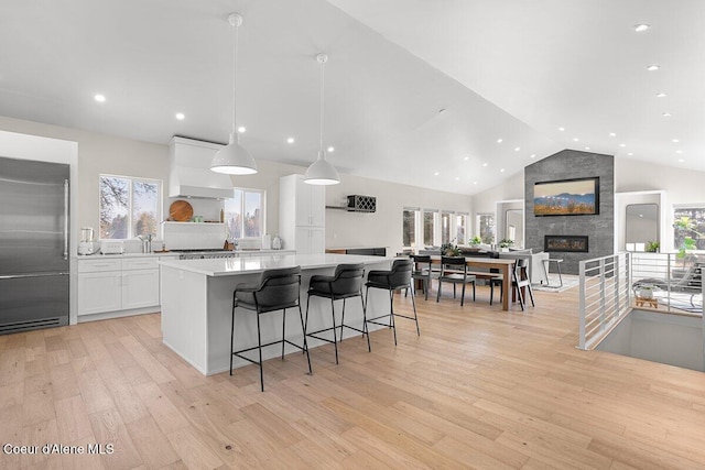 kitchen with stainless steel built in refrigerator, white cabinets, custom range hood, light hardwood / wood-style floors, and hanging light fixtures