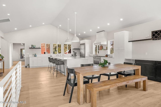 dining area featuring light wood-type flooring and high vaulted ceiling