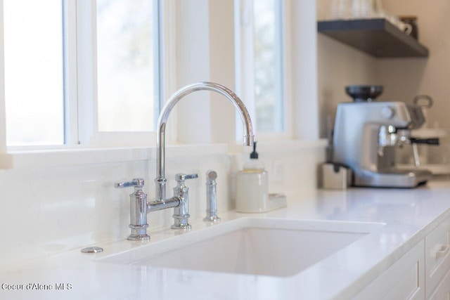 interior details featuring white cabinets, light stone counters, and sink