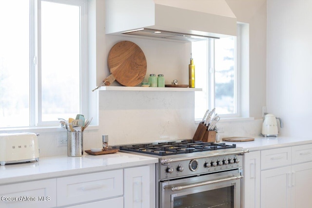 kitchen featuring light stone countertops, white cabinetry, wall chimney exhaust hood, and high end range