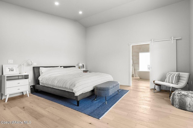 bedroom featuring light hardwood / wood-style floors, ensuite bathroom, and vaulted ceiling