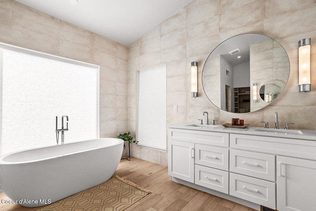 bathroom with lofted ceiling, tile walls, hardwood / wood-style floors, a washtub, and vanity