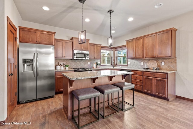 kitchen featuring a kitchen island, hanging light fixtures, light stone countertops, a breakfast bar area, and stainless steel appliances