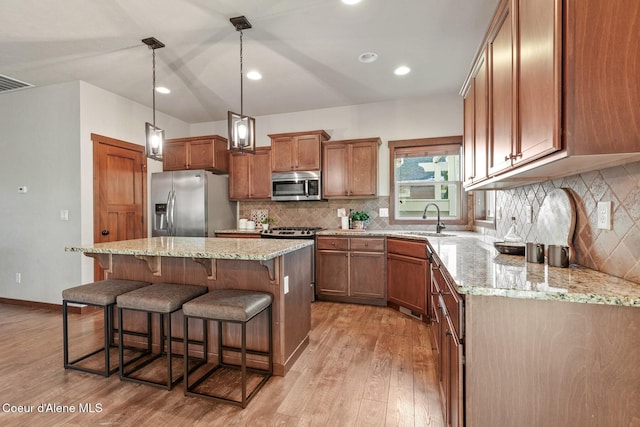 kitchen featuring pendant lighting, appliances with stainless steel finishes, a kitchen island, light hardwood / wood-style floors, and sink