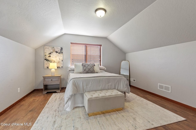 bedroom with vaulted ceiling, a textured ceiling, and hardwood / wood-style floors