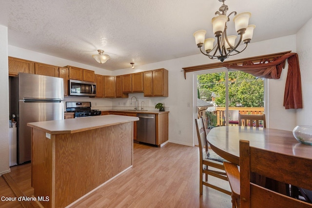 kitchen featuring appliances with stainless steel finishes, light hardwood / wood-style floors, a center island, a notable chandelier, and pendant lighting